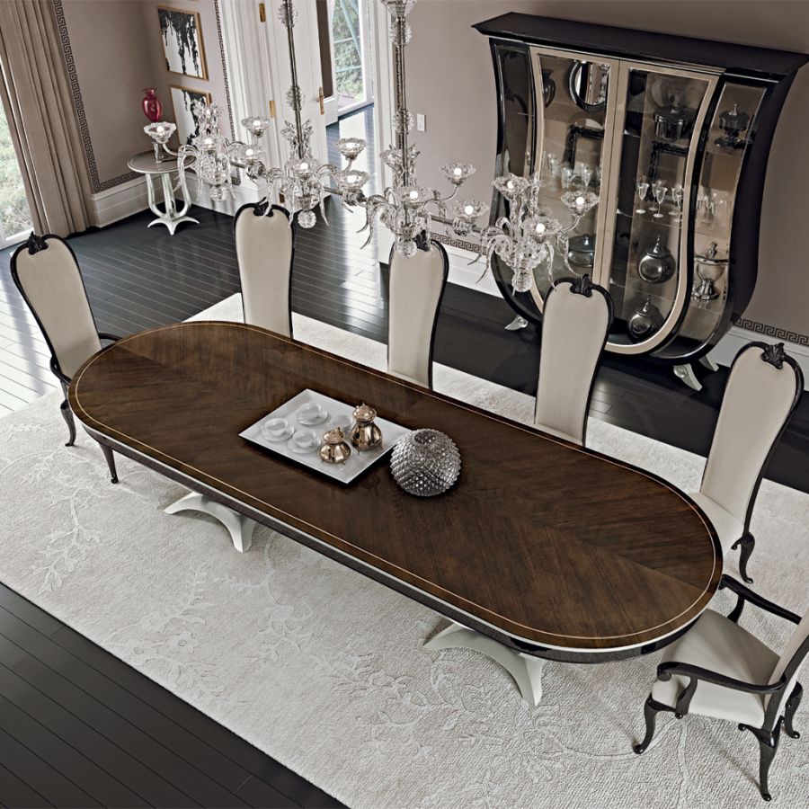 A luxurious prestige dining room setting by Modenese, featuring a long, high-gloss dark wood table surrounded by elegant cream upholstered chairs with classic curved backs.